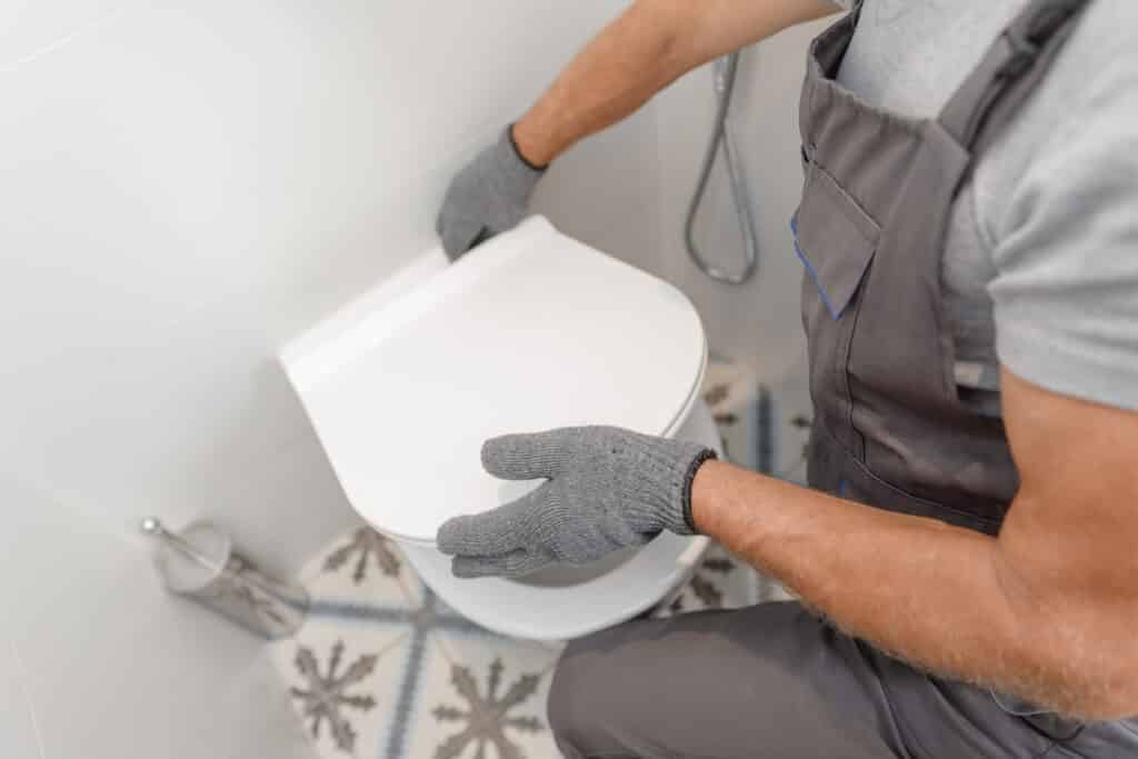 Plombier expert : Installation et entretien de WC modernes Mains gantées d'un plombier ajustant le siège de toilettes blanches. Scène de salle de bain moderne avec carrelage.